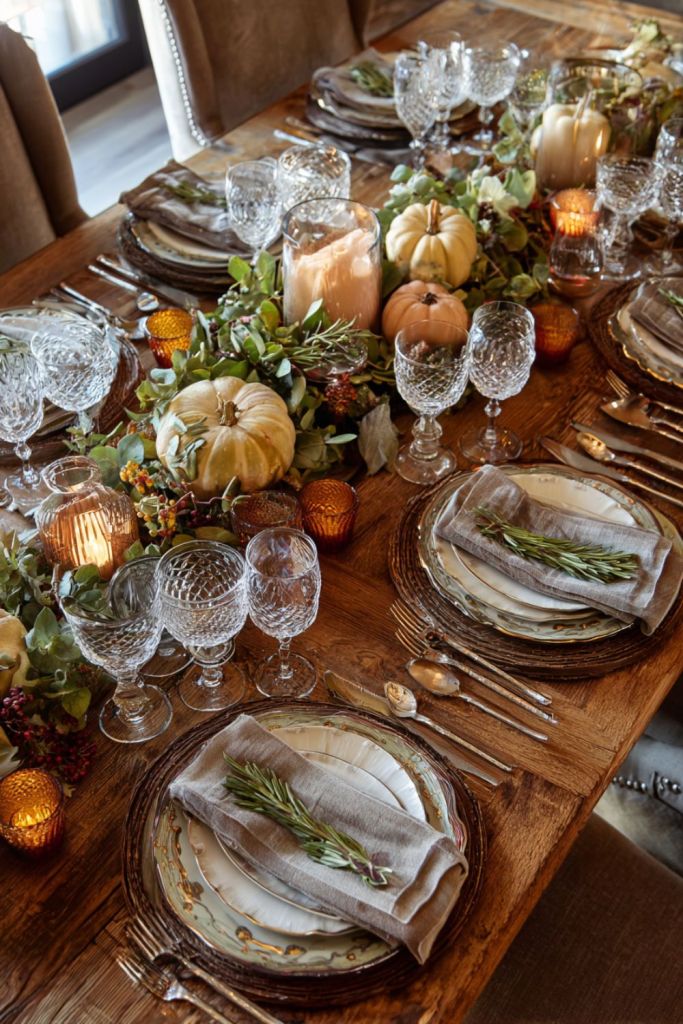 a rustic wooden dining table adorned with pumpkins, candles, glassware, and autumnal decor, set for an elegant meal-thanksgiving table decor-loves from bet 