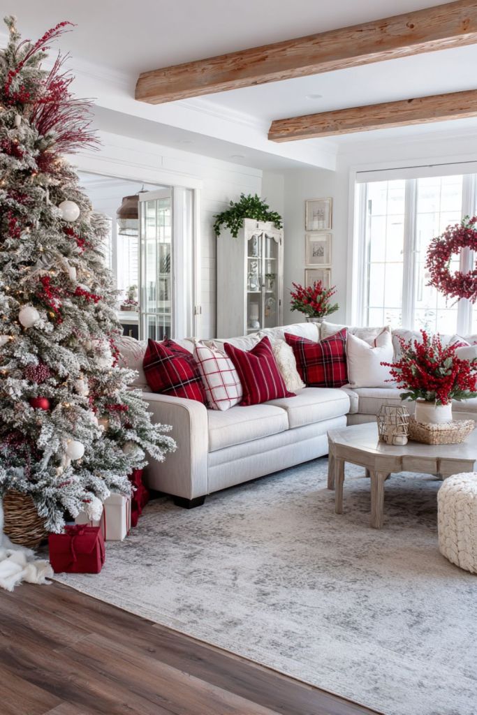 Bright Christmas living room with red plaid pillows, flocked tree with red and white ornaments, and white sofa under wooden ceiling beams.